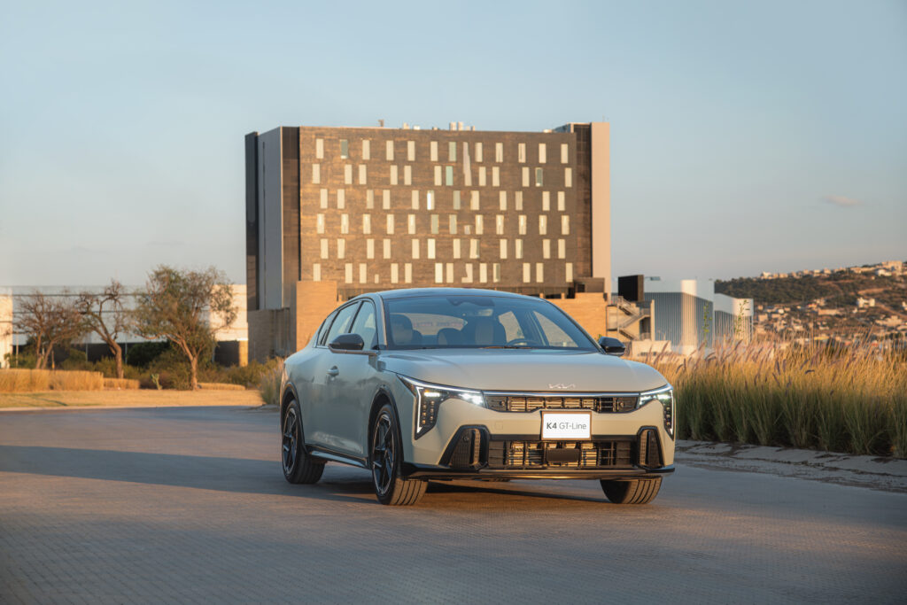Sedán compacto Kia K4 color gris con diseño fastback circulando en ciudad, ganador del premio MotorWeek 2026.